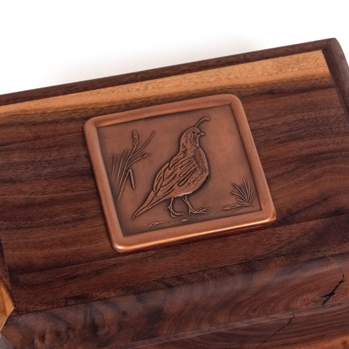 A close-up of a Heritage humidor featuring a raised copper-toned metal plaque with an engraved quail.