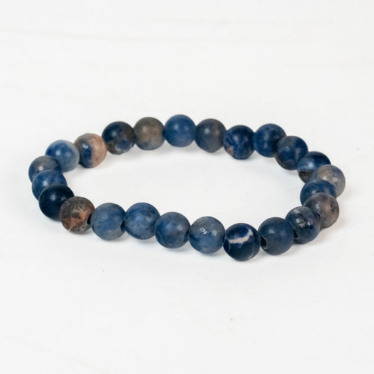 A beaded stretch bracelet made of matte, round dark blue beads with some natural brown and gray marbling, displayed on a clean white background.