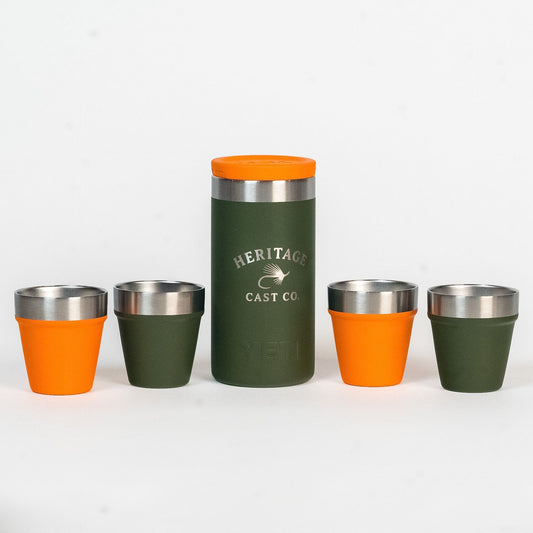 A set of five insulated shot glasses and one matching tumbler from Heritage Cast Co. The set features dark green and bright orange color blocking with stainless steel rims, arranged on a clean white background.