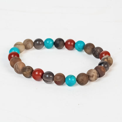 A beaded stretch bracelet made of round wooden beads in various natural brown tones, with a few turquoise blue and red beads, displayed on a clean white background.